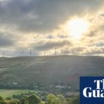 A view across a valley towards sunlit hills with wind turbines and a village off to the left